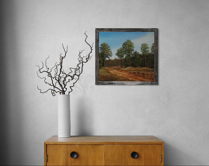Pu&ograve; includere: Un dipinto di paesaggio incorniciato raffigura uno stradone che conduce in una foresta con alberi verdi sotto un cielo blu. Il dipinto ha una cornice in legno rustica e usurata. Un vaso bianco con rami scuri &egrave; su un mobile di legno.