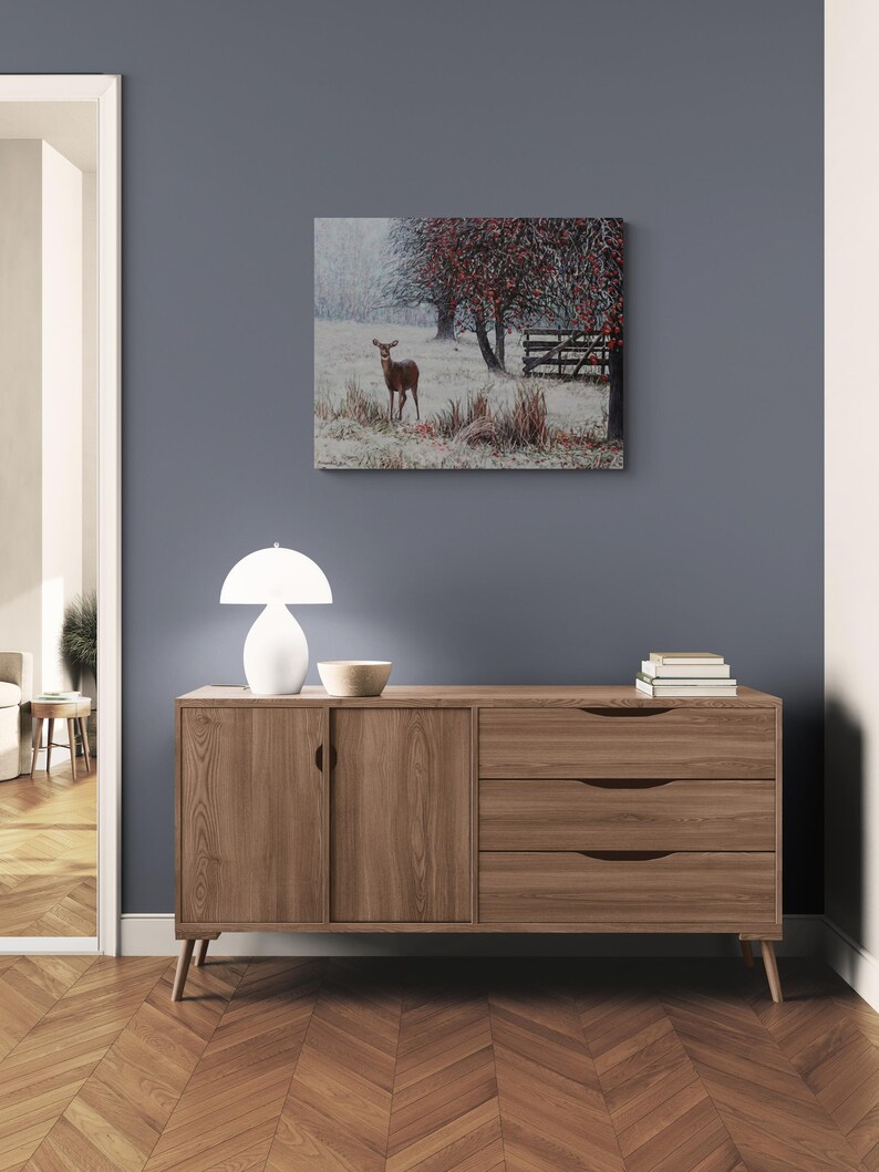 Pu&ograve; includere: Una credenza in legno chiaro con due ante e tre cassetti. Una lampada bianca e una piccola ciotola sono sopra. Un dipinto di un cervo in un campo innevato &egrave; appeso al muro. La credenza &egrave; lunga 150 cm.