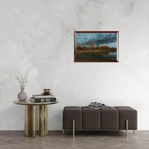 Pu&ograve; includere: Un dipinto di paesaggio incorniciato raffigura un sereno paesaggio acquatico sotto un cielo drammatico e nuvoloso. L'opera d'arte, con una cornice in legno scuro, presenta un lago riflettente, alberi e una tavolozza di colori cupi di blu, marroni e arancioni. Il dipinto &egrave; esposto su una parete bianca.