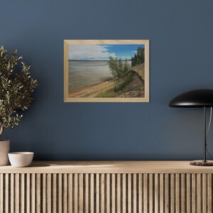K&ouml;nnte beinhalten: Gerahmtes Landschaftsgem&auml;lde, das eine Szene am Wasser zeigt. Das Kunstwerk zeigt einen sandigen Uferbereich, &uuml;ppige gr&uuml;ne Vegetation und ein Gew&auml;sser unter einem bew&ouml;lkten Himmel mit blauen Flecken. Das Gem&auml;lde befindet sich in einem Holzrahmen.
