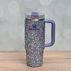 May include: A stainless steel tumbler with a purple lid and handle. The tumbler is covered in iridescent rhinestones.