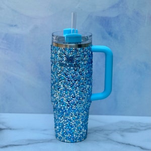 May include: A blue stainless steel tumbler with a handle and a straw. The tumbler is covered in blue and white rhinestones.