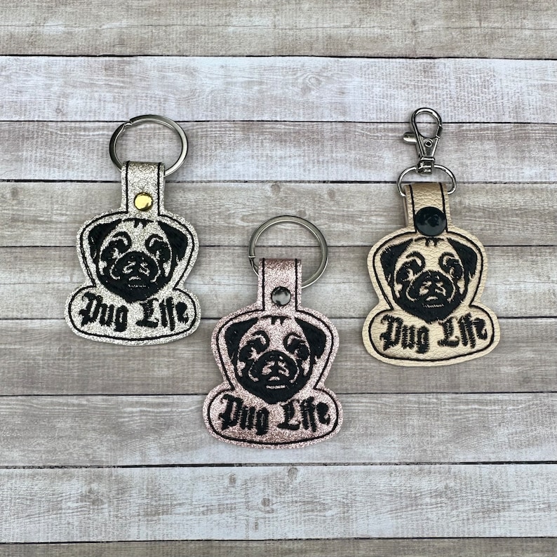 Peut inclure: Trois porte-cl&eacute;s avec un visage de carlin et le texte "Pug Life" en lettres noires. Les porte-cl&eacute;s sont en mat&eacute;riau paillet&eacute; argent, or et rose.
