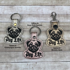 Peut inclure: Trois porte-cl&eacute;s en cuir avec un visage de carlin et le texte "Pug Life" brod&eacute; en noir. Les porte-cl&eacute;s ont une finition scintillante. Les porte-cl&eacute;s sont disponibles en trois couleurs&nbsp;: champagne scintillant, or rose scintillant et or m&eacute;tallis&eacute;.