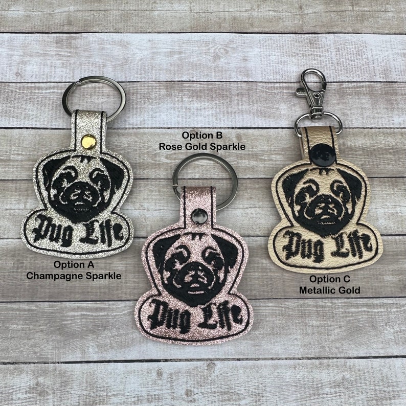Peut inclure: Trois porte-cl&eacute;s en cuir avec un visage de carlin et le texte "Pug Life" brod&eacute; en noir. Les porte-cl&eacute;s ont une finition scintillante. Les porte-cl&eacute;s sont disponibles en trois couleurs&nbsp;: champagne scintillant, or rose scintillant et or m&eacute;tallis&eacute;.