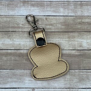 Peut inclure: Un porte-cl&eacute;s en cuir de couleur dor&eacute;e avec un bouton noir et un fermoir en m&eacute;tal argent&eacute;. Le porte-cl&eacute;s a la forme d'un nuage.