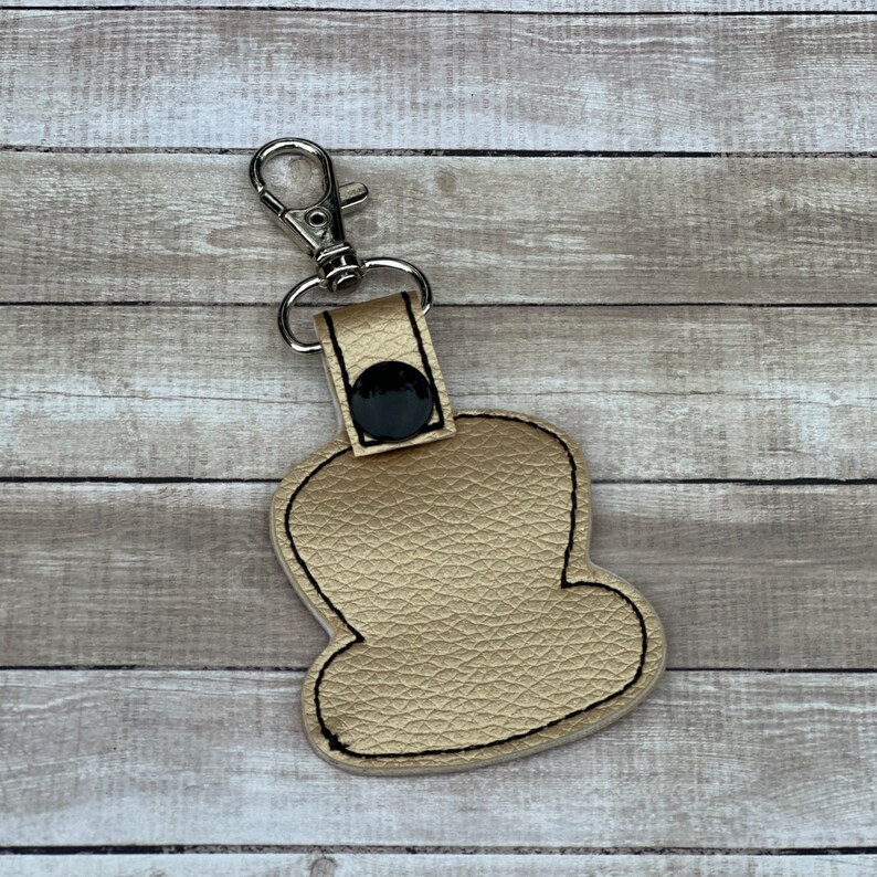 Peut inclure: Un porte-cl&eacute;s en cuir de couleur dor&eacute;e avec un bouton noir et un fermoir en m&eacute;tal argent&eacute;. Le porte-cl&eacute;s a la forme d'un nuage.