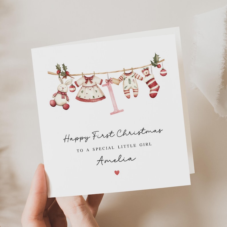 May include: A Christmas card with a watercolor illustration of a clothesline with baby clothes and a bunny. The text reads "Happy First Christmas to a special little girl Amelia".