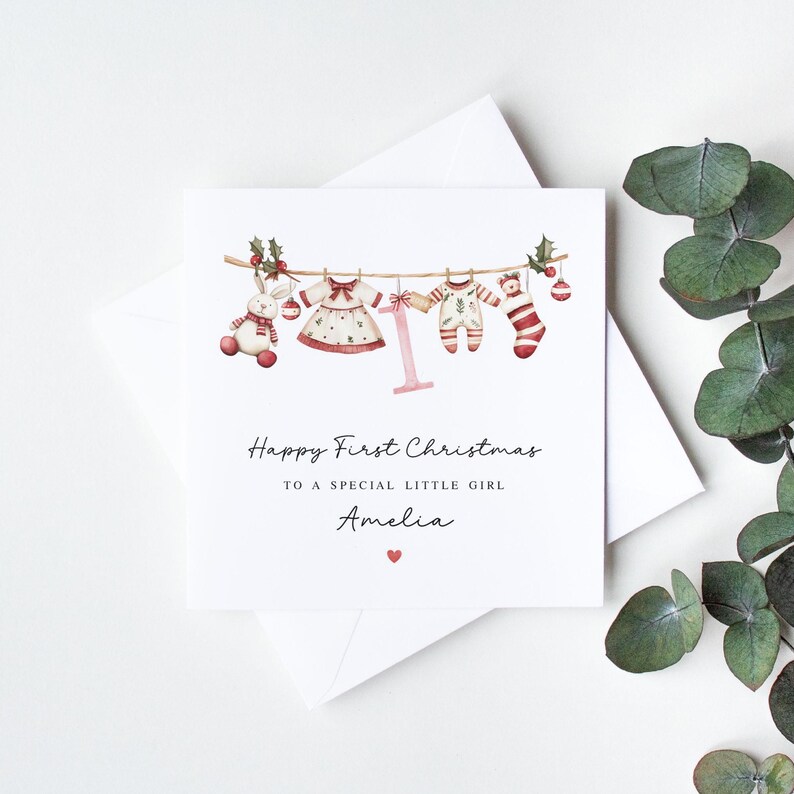 May include: A Christmas card with a watercolor illustration of baby clothes hanging on a line. The card says "Happy First Christmas to a special little girl Amelia".