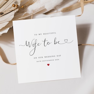 May include: A white card with elegant script that reads "To My Beautiful Wife to be" and "On Our Wedding Day 24th September 2024". A small red heart is at the bottom. The card is surrounded by dried flowers.
