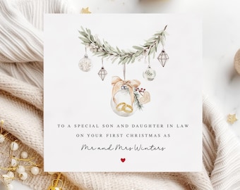 May include: A Christmas card featuring a watercolour illustration of a garland with baubles and a ring inside a glass bauble. The text reads "To a special son and daughter in law on your first Christmas as Mr and Mrs Winters".