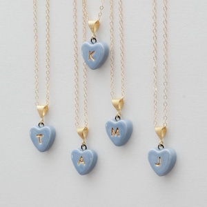 May include: Five delicate gold-tone chain necklaces, each featuring a small, light blue heart-shaped pendant. Each heart pendant is embossed with a single gold-colored letter, specifically the letters T, A, K, M, and J, suspended from a gold bail.