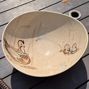 Puede incluir: Un cuenco de cerámica grande, redondo y de color beige moteado, con un diseño pintado de un pájaro marrón con detalles azules en el lado izquierdo y dos pájaros marrones más pequeños en el derecho, junto a dibujos lineales de tallos en azul claro.