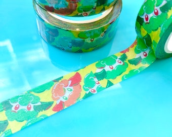 Op de afbeelding: Drie rollen washi tape met een groen, geel en rood patroon van cartoon gezichten. De tape ligt op een blauwe ondergrond.