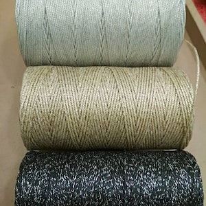 Puede incluir: Tres carretes de hilo, uno plateado, uno dorado y uno negro con destellos plateados. El hilo está enrollado firmemente en los carretes.