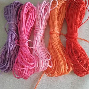 May include: Five spools of embroidery floss in shades of purple, pink, light pink, orange, and red.
