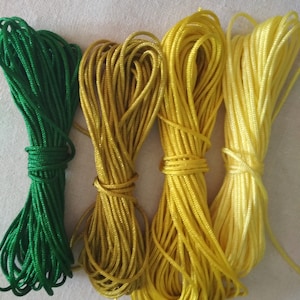 May include: Four spools of cord in shades of green, yellow, and light yellow.