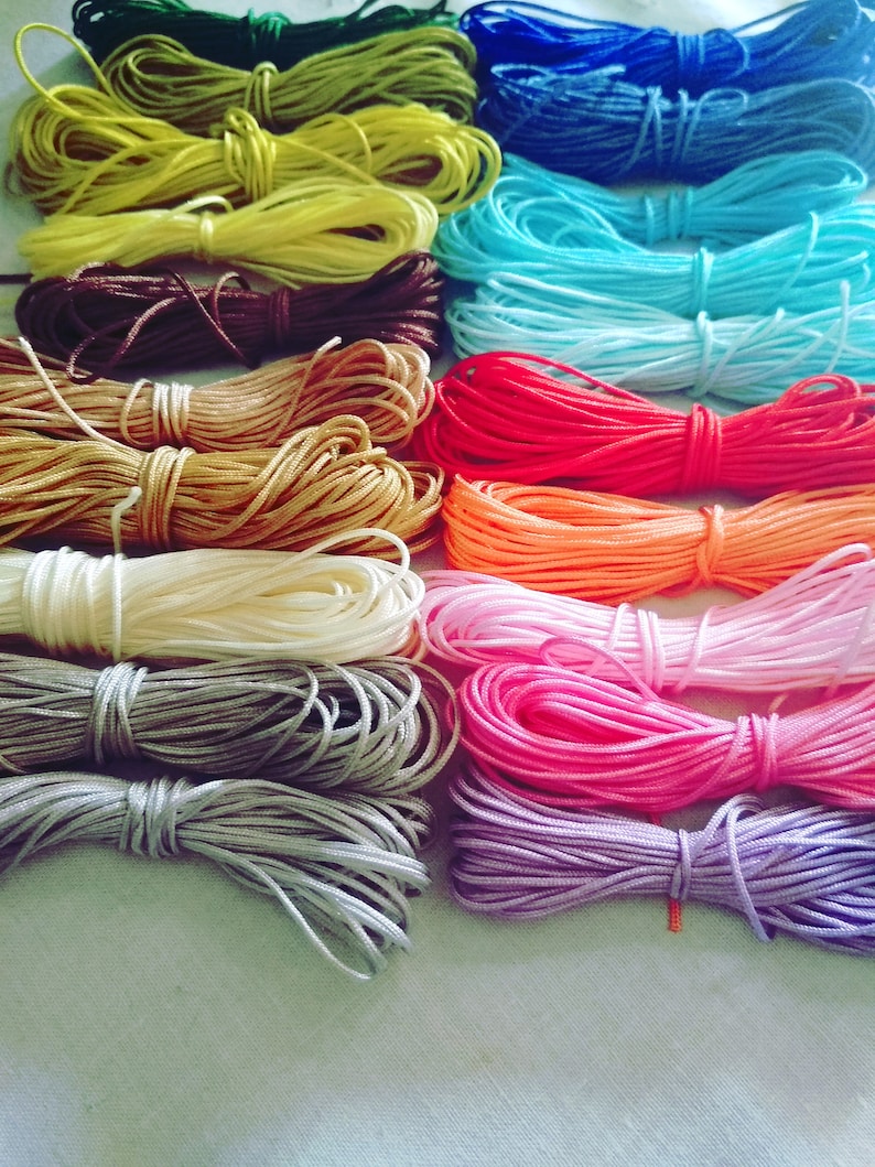 May include: A collection of 15 spools of colorful waxed cotton cord. The cords are arranged in rows, with each row featuring a different color. The colors include green, yellow, brown, gold, white, gray, pink, purple, blue, turquoise, orange, red, and black.