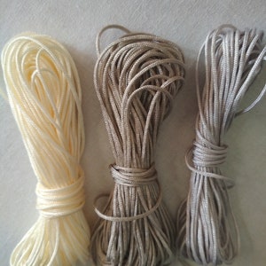 May include: Three spools of cord in different shades of beige. The cord is wound tightly and is ready for crafting projects.