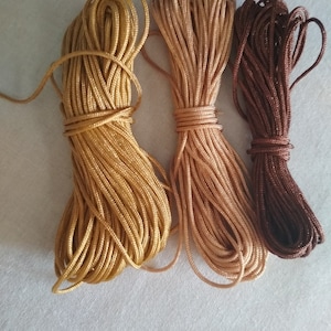 May include: Three spools of cord in different shades of brown. The cord is tightly wound and ready for crafting projects.