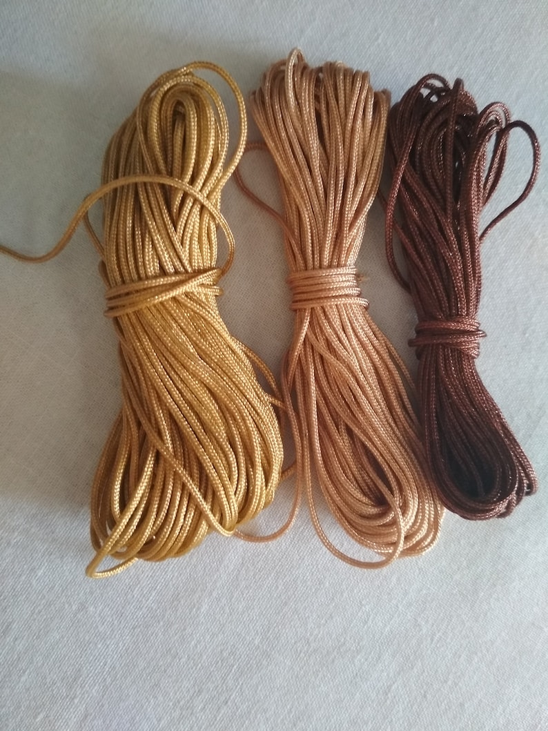 May include: Three spools of cord in different shades of brown. The cord is tightly wound and ready for crafting projects.