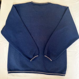 May include: A navy blue long-sleeve sweatshirt featuring a crew neckline with a subtle grey striped trim. The garment includes matching grey striped detailing on the sleeve cuffs and the bottom hem, providing a consistent look across the piece.