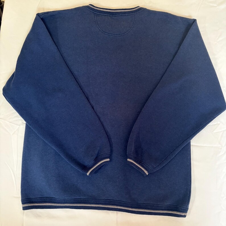 May include: A navy blue long-sleeve sweatshirt featuring a crew neckline with a subtle grey striped trim. The garment includes matching grey striped detailing on the sleeve cuffs and the bottom hem, providing a consistent look across the piece.