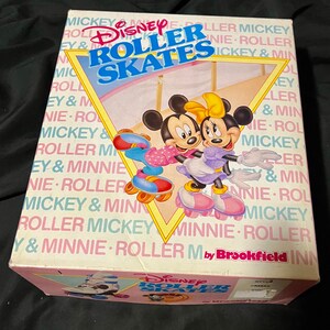 May include: A pink and white box with a picture of Mickey Mouse and Minnie Mouse roller skating. The box says "Disney Roller Skates" and "by Brookfield".