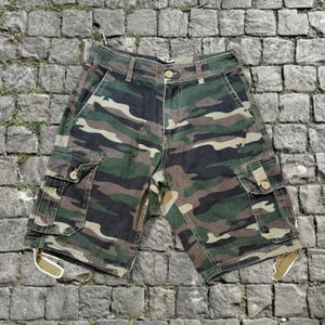 May include: Camouflage cargo shorts in shades of green, brown, and black. The shorts have multiple pockets, a button closure, and belt loops. The shorts are made of a durable fabric and are suitable for outdoor activities.