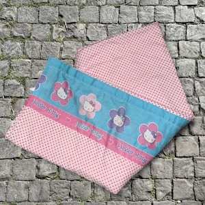 May include: Two-piece Hello Kitty bedding set. The set includes a pink polka-dot pillowcase and a pillowcase with a blue border. The blue border features Hello Kitty in flower designs and the text "Hello Kitty".
