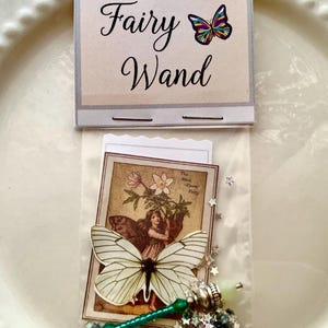 May include: A miniature fairy wand set in a clear plastic bag. The set includes a wand with a green handle and silver accents, a butterfly, a vintage-style illustration, and star-shaped confetti. The packaging reads "Magical Miniature Fairy Wand."
