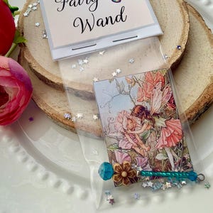May include: A clear plastic bag containing a fairy wand with a blue bead, a brown flower-shaped bead, and a green beaded handle. The packaging features a card labeled Magical Miniature Fairy Wand with a butterfly and a fairy illustration.