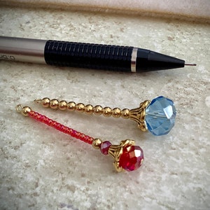 May include: Two gold-toned wands with crystal tips. The top wand has a light blue crystal tip and the bottom wand has a red crystal tip.