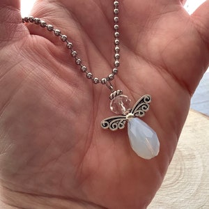 May include: A silver chain necklace with a clear crystal bead and a silver angel pendant with a light blue gemstone.