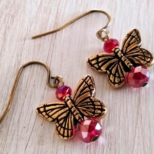 May include: Gold butterfly earrings with red crystal accents. The butterflies have detailed wings and the crystals are faceted.
