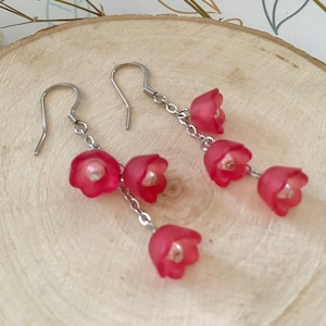 May include: A pair of silver dangle earrings with four pink flower-shaped charms on each earring.