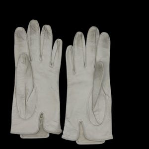 May include: A pair of off-white leather gloves. The gloves have a classic design with individual finger slots and a split at the wrist. The stitching is visible, and the gloves appear to be well-worn.