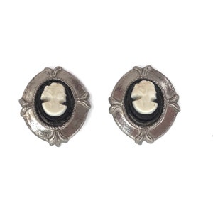 May include: A pair of silver tone earrings with black and white cameo insets. The cameos feature a woman's profile.