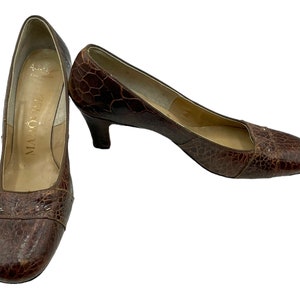 May include: A pair of brown leather pumps with a low heel. The shoes have a textured, crocodile-embossed design and a small, decorative detail on the toe. The shoes are labeled "Malouf" on the insole.