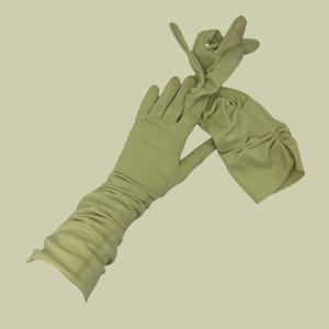 Könnte beinhalten: Ein Paar lange, hellgrüne Handschuhe. Die Handschuhe sind aus einem weichen, dehnbaren Material gefertigt und haben ein gerafftes Design am Unterarm. Die Handschuhe werden vor einem hellgrünen Hintergrund gezeigt.