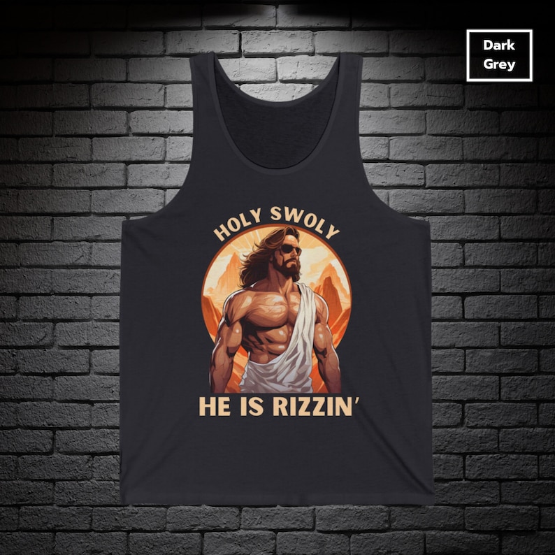 Puede incluir: Una camiseta sin mangas de color gris oscuro con un gr&aacute;fico de una figura musculosa de Jes&uacute;s con gafas de sol y una t&uacute;nica blanca. El gr&aacute;fico est&aacute; rodeado de un c&iacute;rculo con el texto "HOLY SWOLY" en la parte superior y "HE IS RIZZIN'" en la parte inferior.
