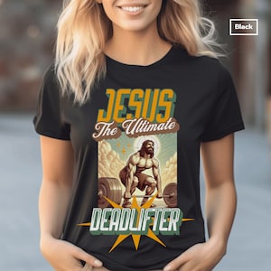 Op de afbeelding: Zwart T-shirt met een afbeelding van Jezus die gewichten heft. De tekst "Jesus The Ultimate Deadlifter" staat op het shirt gedrukt.