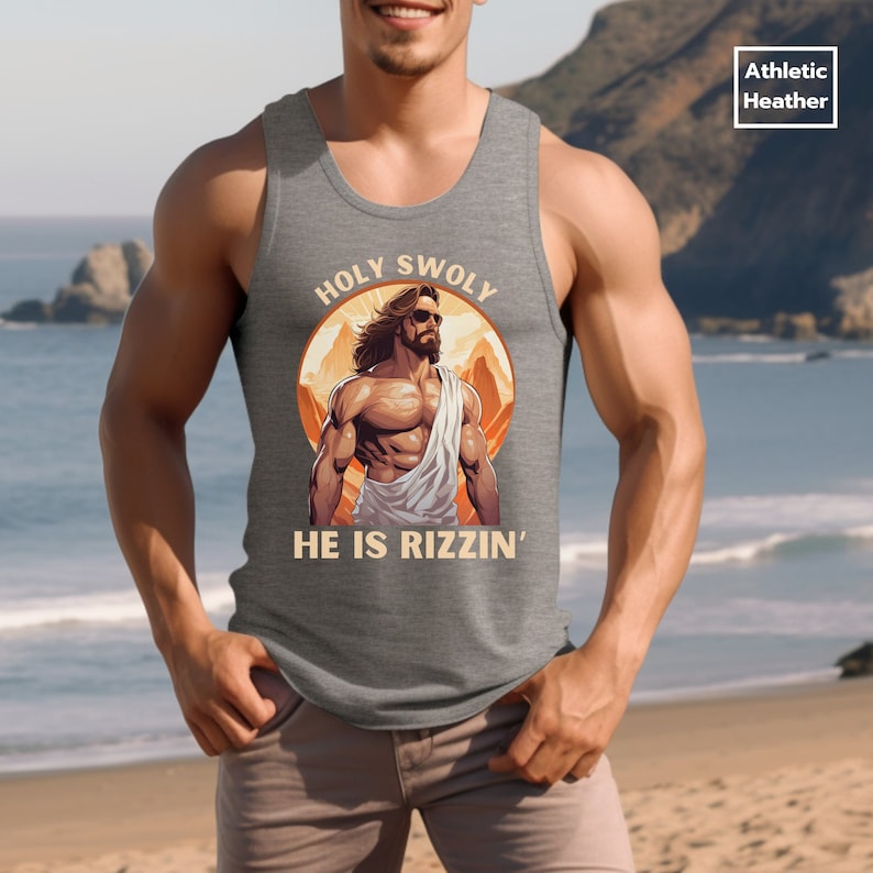 Puede incluir: Una camiseta sin mangas gris con un gr&aacute;fico de una figura musculosa de Jes&uacute;s con gafas de sol y una t&uacute;nica. El gr&aacute;fico est&aacute; rodeado de un c&iacute;rculo con el texto "HOLY SWOLY" en la parte superior y "HE IS RIZZIN'" en la parte inferior.