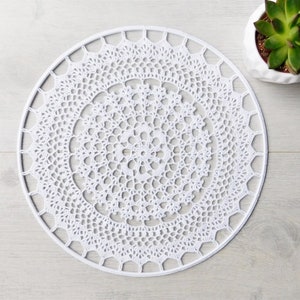 May include: White crocheted doily with a circular design. The doily has a delicate lace pattern and is perfect for adding a touch of elegance to any home.