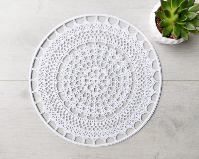 May include: White crocheted doily with a circular design. The doily has a delicate lace pattern and is perfect for adding a touch of elegance to any home.