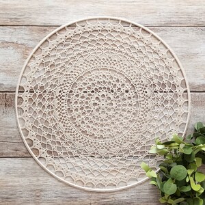 May include: A large, white crocheted doily with a circular design. The doily is hanging on a wooden wall.