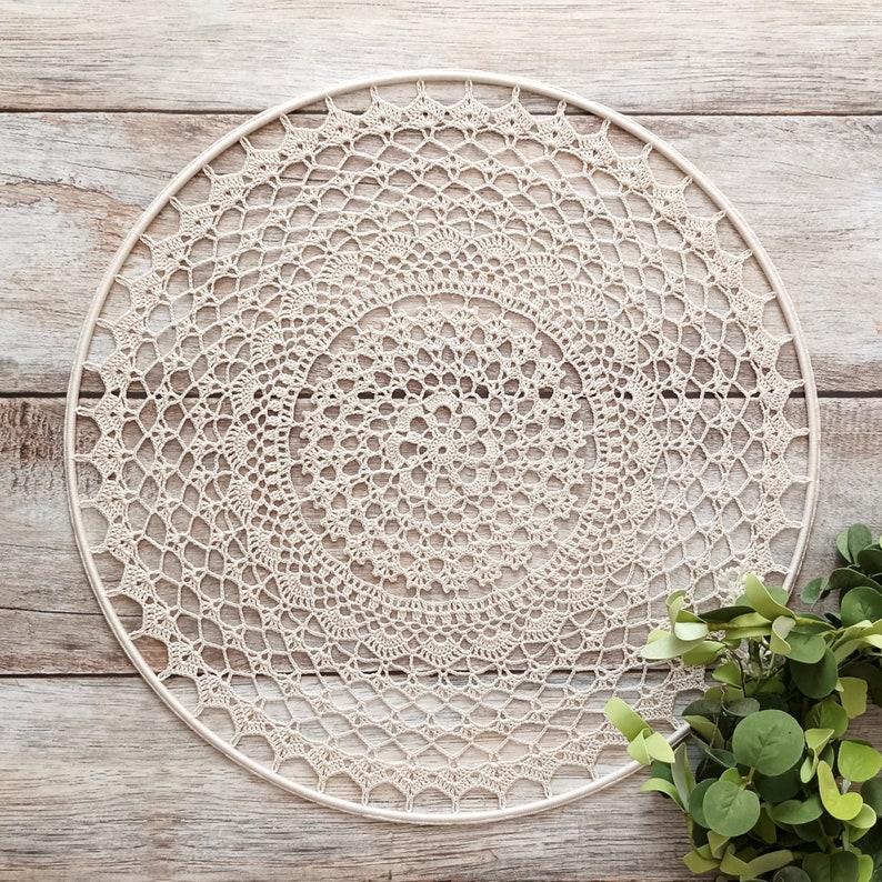 May include: A large, white crocheted doily with a circular design. The doily is hanging on a wooden wall.