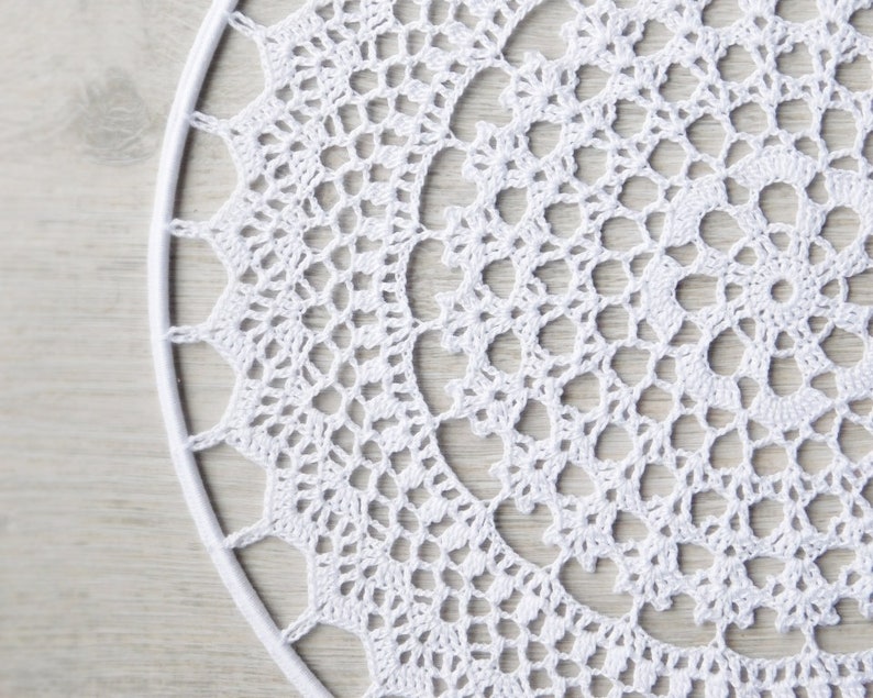 May include: White crochet doily with a circular design. The doily is made of delicate, intricate stitches and has a lacy appearance.