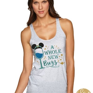 May include: A white tank top with a teal and gold glitter design. The design features a wine glass with a Mickey Mouse head and the text "A Whole New Buzz".