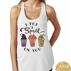 Puede incluir: Camiseta blanca de tirantes con el texto "I put a spell on you" y un gráfico de tres tazas de café con temática de Halloween.